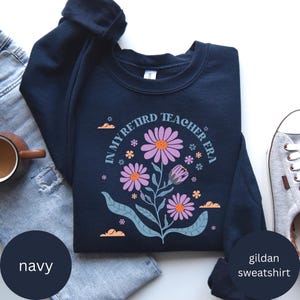 May include: Navy blue Gildan sweatshirt with a floral design and the text "In My Retired Teacher Era".