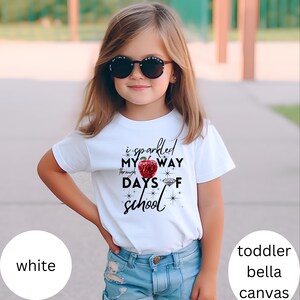 May include: White toddler t-shirt with a red apple graphic and the text "I sparkled my way through days of school".