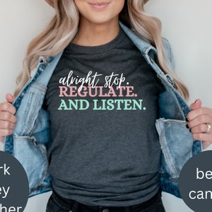 May include: A dark heather grey t-shirt with the text "alight stop. REGULATE. AND LISTEN." in pink and teal lettering.