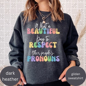 以下が含まれることがあります： レインボーカラーで「What a beautiful day to respect other people's pronouns」と書かれたダークヘザーグレーのスウェットシャツです。
