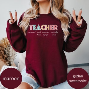 May include: Maroon Gildan sweatshirt with the word "TEACHER" spelled out in colorful letters. The letters are defined as "consonant, vowel, consonant, r-controlled, team digraph, vowel".