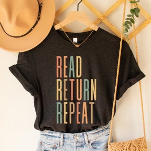 May include: A dark grey t-shirt with the text "READ RETURN REPEAT" in colourful retro-style lettering.