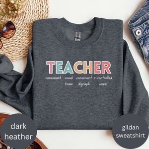 May include: Dark heather grey Gildan sweatshirt with the word "TEACHER" in colorful letters. The word is broken down into its parts of speech: consonant, vowel, consonant, r-controlled vowel, team, digraph.