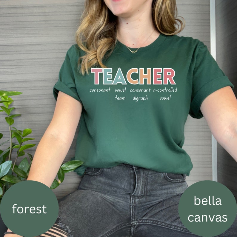May include: A green t-shirt with the word "TEACHER" written in colorful letters. The word is broken down into its phonetic parts: consonant, vowel, consonant, r-controlled vowel, team, digraph.