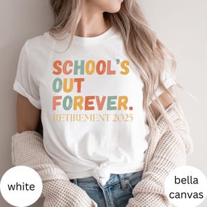 May include: White t-shirt with the text "SCHOOL'S OUT FOREVER. RETIREMENT 2025" in orange, green, and yellow. The shirt is made of a soft material and is a Bella + Canvas brand.