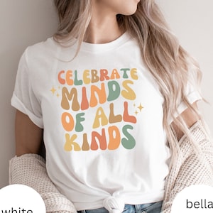 May include: White t-shirt featuring a retro-style graphic that reads "Celebrate Minds of All Kinds" in colourful, wavy lettering.