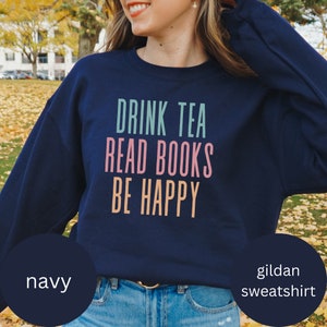 Puede incluir: Sudadera azul marino Gildan con el texto "Drink Tea Read Books Be Happy" en letras de colores.