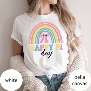 Może przedstawiać: Biała koszulka Bella Canvas z tęczowym wzorem i napisem "3.14 Happy Pi Day". Projekt zawiera symbol pi i datę 3.14. Koszulka jest w stylu casual.
