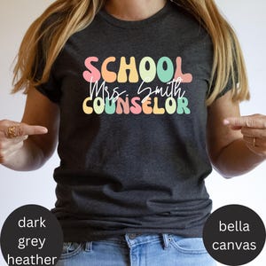 May include: Dark heather grey t-shirt with the text "SCHOOL Mrs. Smith COUNSELOR" in rainbow colors.