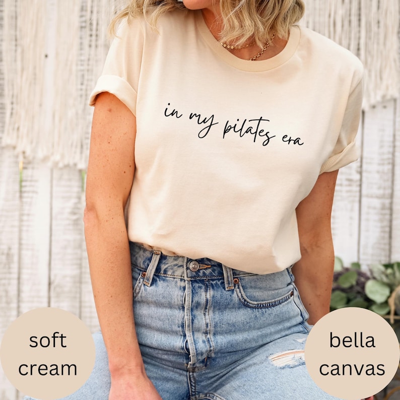 Pu&ograve; includere: T-shirt color crema con la scritta "in my pilates era" in corsivo nero. La maglietta &egrave; realizzata in morbido materiale Bella Canvas color crema. La modella indossa jeans blu.