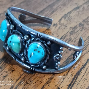 May include: A silver cuff bracelet with three turquoise stones set in a decorative design.