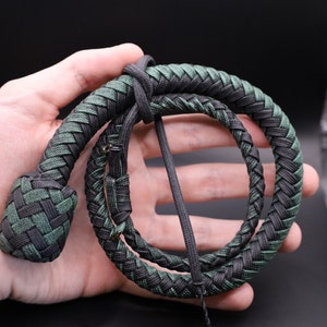 May include: A braided whip in shades of green and black, coiled in a loop. The whip's handle is a tightly woven knot, and the body is a series of interwoven strands. The overall design is symmetrical and detailed.