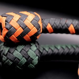 May include: Close-up of a braided object with a black and orange color scheme. The top section is orange and black, while the bottom section is green and black. The object appears to be a decorative knot or part of a larger item.