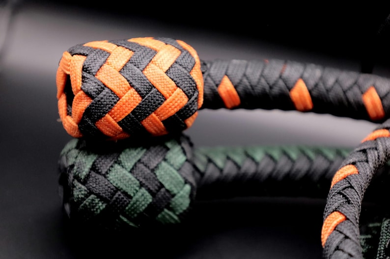 May include: Close-up of a braided object with a black and orange color scheme. The top section is orange and black, while the bottom section is green and black. The object appears to be a decorative knot or part of a larger item.