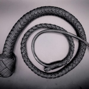 May include: A black and gray braided whip, coiled in a spiral. The whip's handle is knotted, and the body is tightly woven. The design is simple and elegant, with a focus on texture and form. The overall aesthetic is dark and mysterious.