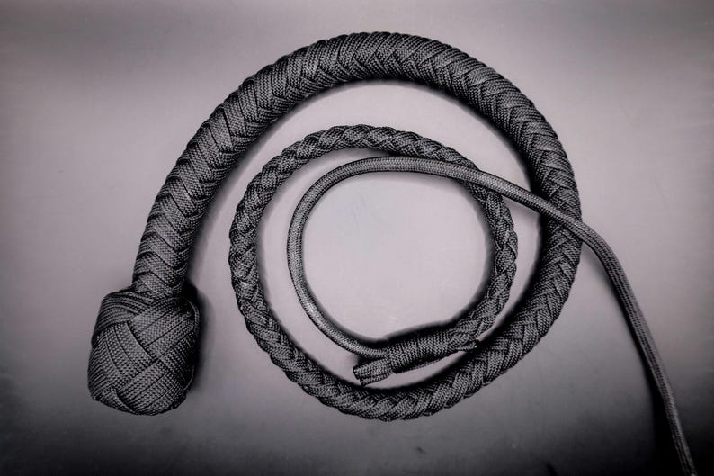 May include: A black and gray braided whip, coiled in a spiral. The whip's handle is knotted, and the body is tightly woven. The design is simple and elegant, with a focus on texture and form. The overall aesthetic is dark and mysterious.