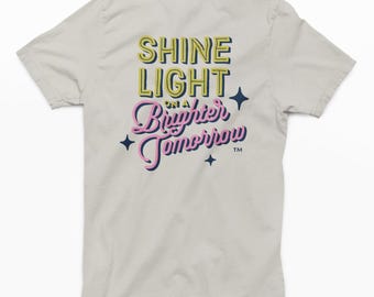 Camiseta beige Shine Light on a Brighter Tomorrow: logotipo Sunshine en la parte delantera, estampado rosa y verde vibrante en la parte posterior, camiseta suave de manga corta