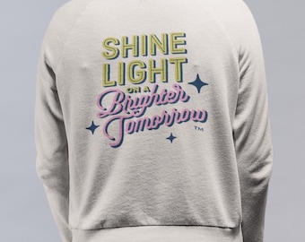 Shine Light on a Brighter Tomorrow - Sudadera de cuello redondo beige, logotipo Sunshine en la parte delantera y gráfico rosa y verde vibrantes en la parte posterior
