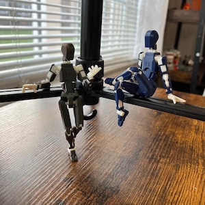 May include: Two articulated action figures posed on a tripod stand. The figure on the left is black and white, while the figure on the right is blue and white.