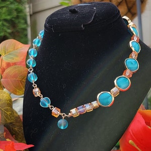 Op de afbeelding: Een turquoise en gouden ketting met een traanvormige hanger. De ketting is gemaakt van glazen kralen en een gouden ketting.