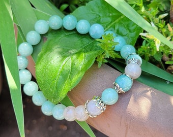 Puede incluir: Un brazalete de cuentas azul claro y blanco con detalles plateados. El brazalete está hecho de cuentas redondas y tiene un diseño floral en los detalles plateados.