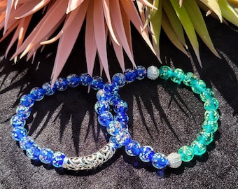 May include: Two beaded bracelets with silver accents. One bracelet is blue and the other is green.