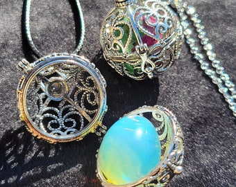 May include: Two silver cage pendants with different colored stones inside. One pendant has a green and pink stone, the other has a blue and yellow stone.