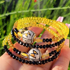 Könnte beinhalten: Ein Set aus drei Armbändern mit schwarzen und gelben Perlen. Die Armbänder haben ein einzigartiges Design mit weißen und gelben Keramikperlen.