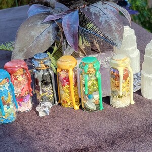 May include: A collection of small glass bottles filled with colorful contents and sealed with wax. The wax on the bottles is in various colors, including blue, red, black, yellow, and green. Two selenite towers are also present.