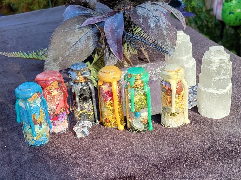 May include: A collection of small glass bottles filled with colorful contents and sealed with wax. The wax on the bottles is in various colors, including blue, red, black, yellow, and green. Two selenite towers are also present.