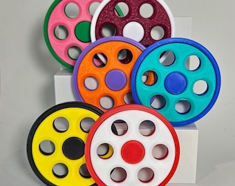May include: A collection of colorful, circular objects with multiple holes, resembling wheels or gears. The objects are in various colors, including pink, green, purple, orange, blue, yellow, red, and white. Each has a central circular accent in a contrasting color.