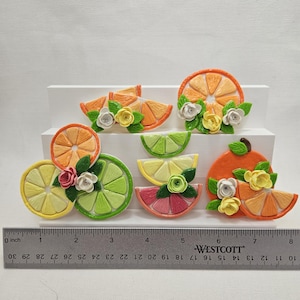May include: A collection of handcrafted fruit slice ornaments, including orange, lemon, lime, and grapefruit, each adorned with small floral accents. The ruler shows a length of 8 inches.