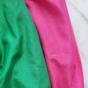 Peut inclure: Deux morceaux de tissu sont présentés côte à côte. L'un est d'un vert vif et uni avec une texture lisse et légèrement réfléchissante. L'autre est d'un rose magenta vif et uni avec un aspect lisse et doux similaire au premier tissu.