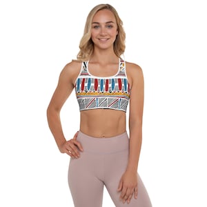 May include: A white sports bra with a colorful geometric pattern. The pattern features red, blue, yellow, and black geometric shapes. The bra has a racerback style.