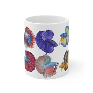 May include: White ceramic mug with a colorful design of multiple betta fish. The fish are painted in shades of blue, red, yellow, and orange.