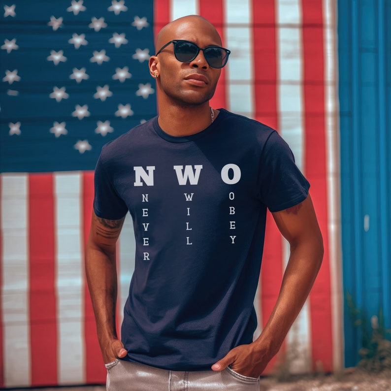 May include: A navy blue t-shirt with white text that reads "NWO" and "NEVER WILL OBEY". The shirt is being worn by a person standing in front of an American flag.