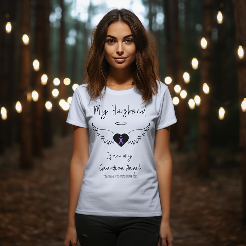 May include: White t-shirt with a black graphic that says "My Husband is now my Guardian Angel" with a purple ribbon and angel wings.