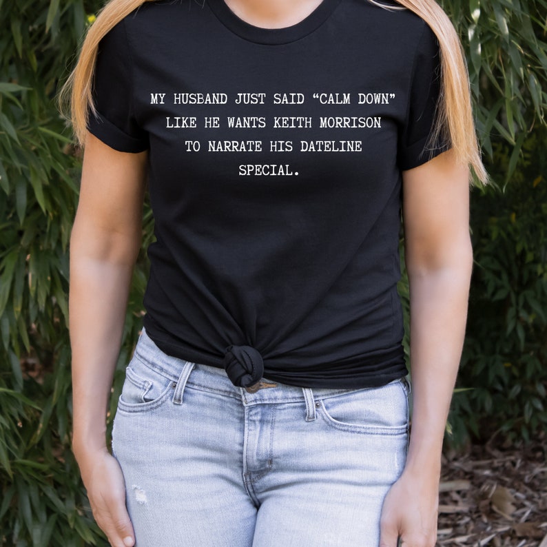 May include: A black t-shirt with white text that reads "MY HUSBAND JUST SAID "CALM DOWN" LIKE HE WANTS KEITH MORRISON TO NARRATE HIS DATELINE SPECIAL."
