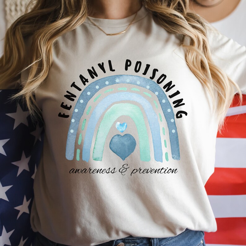 Puede incluir: Una camiseta blanca con un dise&ntilde;o de arco&iacute;ris azul y verde y el texto "FENTANYL POISONING awareness & prevention".