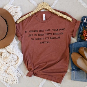 May include: A rust-colored t-shirt with the text "MY HUSBAND JUST SAID "CALM DOWN" LIKE HE WANTS KEITH MORRISON TO NARRATE HIS DATELINE SPECIAL."