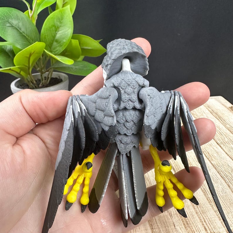 May include: A 3D printed model of a bird with gray and black feathers and yellow feet. The bird is posed with its wings spread out and its tail feathers fanned out.