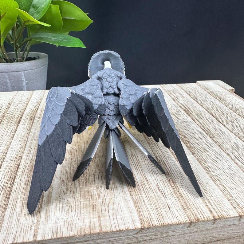 May include: A 3D printed model of a bird with its wings spread out. The bird is gray and has a detailed texture. The model is sitting on a wooden surface.