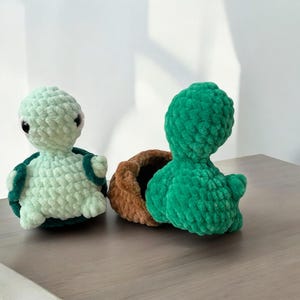 May include: Two crocheted turtle toys. One is green and the other is light green with a brown shell.