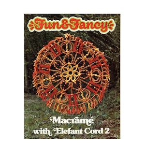 May include: A macrame wall hanging with a circular design featuring a central flower motif. The hanging is made with red, orange, and yellow cord and includes wooden beads. The title "Fun & Fancy" and "Macrame with Elefant Cord 2" are printed on the image.