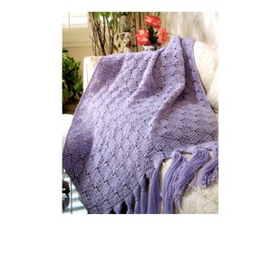 May include: A lavender crochet throw blanket with fringe on a white sofa. The blanket is draped over the sofa and has a delicate, lacy pattern.