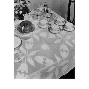 May include: A white crocheted tablecloth with a floral design featuring tulips and leaves. The tablecloth is set with a silver teapot, sugar bowl, creamer, and four teacups and saucers.