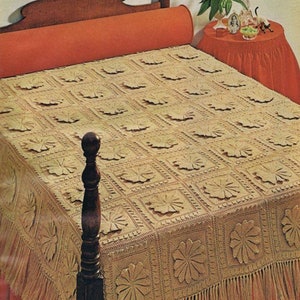 May include: A crocheted bedspread with a floral design in a beige color. The bedspread has a fringe border and is on a bed with a red headboard and a red bolster pillow.