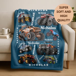 May include: A navy blue blanket featuring colorful monster truck illustrations. The blanket has the name "Nicholas" printed repeatedly. A circular graphic reads "Super Soft and High Quality".