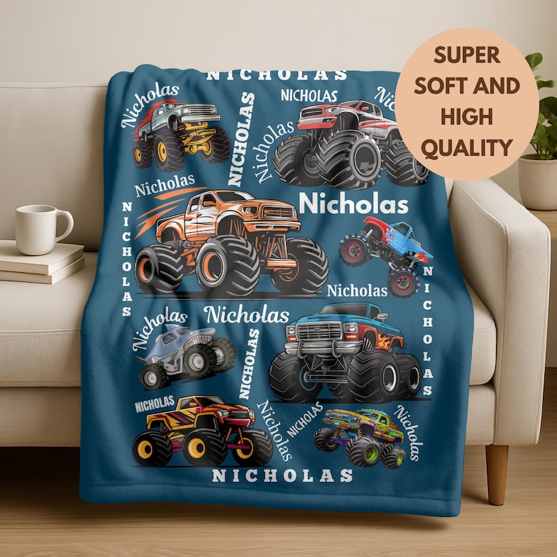 May include: A navy blue blanket featuring colorful monster truck illustrations. The blanket has the name "Nicholas" printed repeatedly. A circular graphic reads "Super Soft and High Quality".