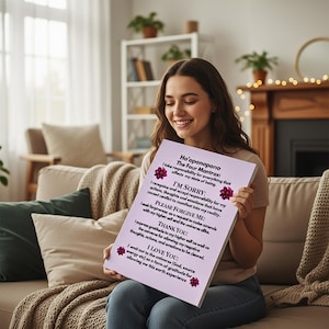 Op de afbeelding: Een vrouw houdt een canvas print vast met de tekst "Ho'oponopono: The Four Mantras". De print heeft een lichtpaarse achtergrond met zwarte tekst en bloemaccenten. De vrouw glimlacht, zittend op een bank in een goed verlichte kamer.